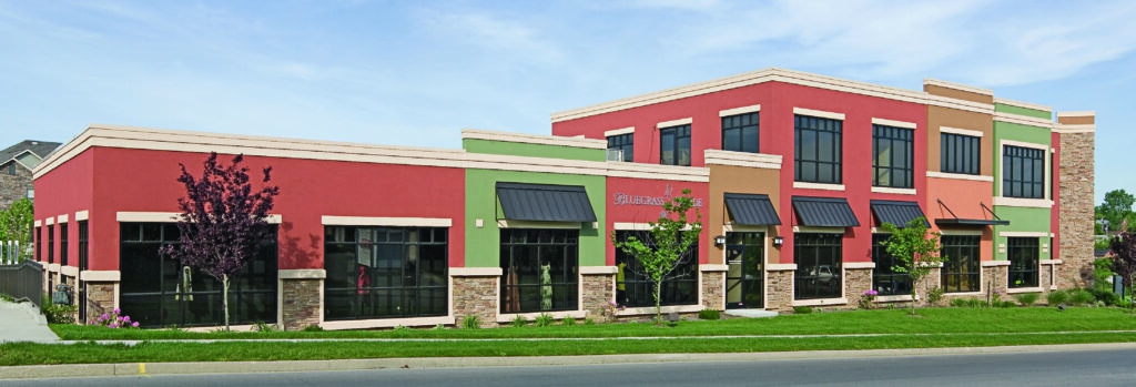 A colorful multi-story commercial building featuring red, green, and tan stucco exteriors with large glass windows and stone accents, built using a Butler Manufacturing PEMB pre-engineered metal building system.